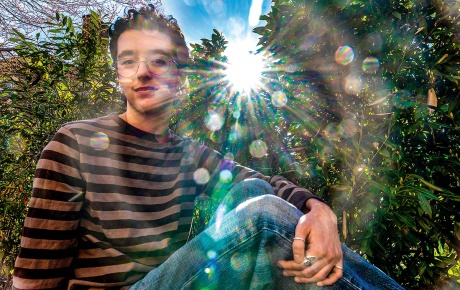 Image of Elliot Stravato sitting with his knee up and the sun shining through the trees
